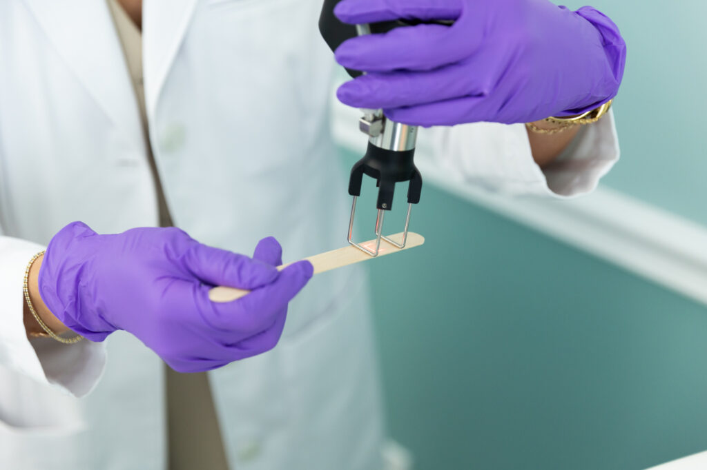 An expert provider shows how laser resurfacing in St. Petersburg works by pointing the laser at a wooden tongue depressor.