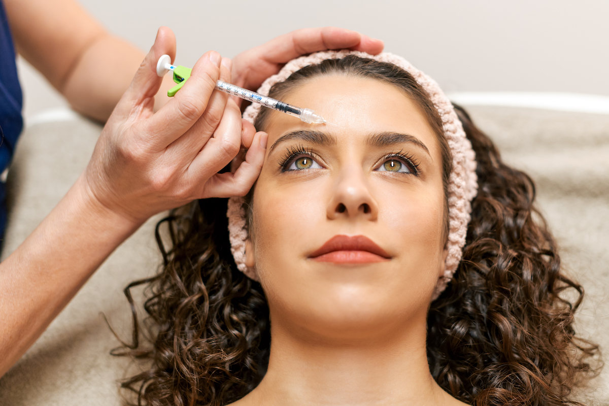 A woman is lying down and receiving botox and laser treatments at Hermann Aesthetics.